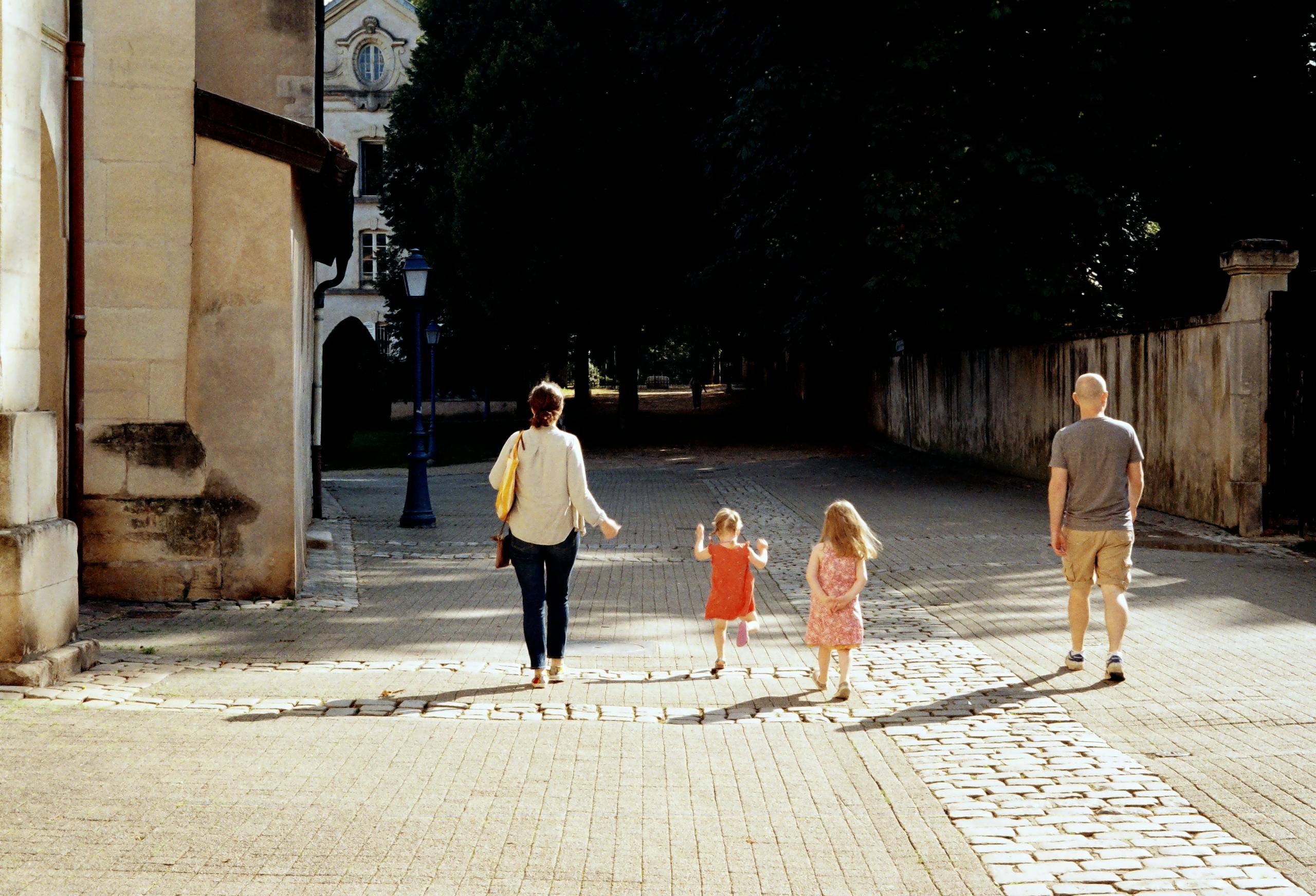 A family of four walks down a picturesque street in France, bathed in sunlight.