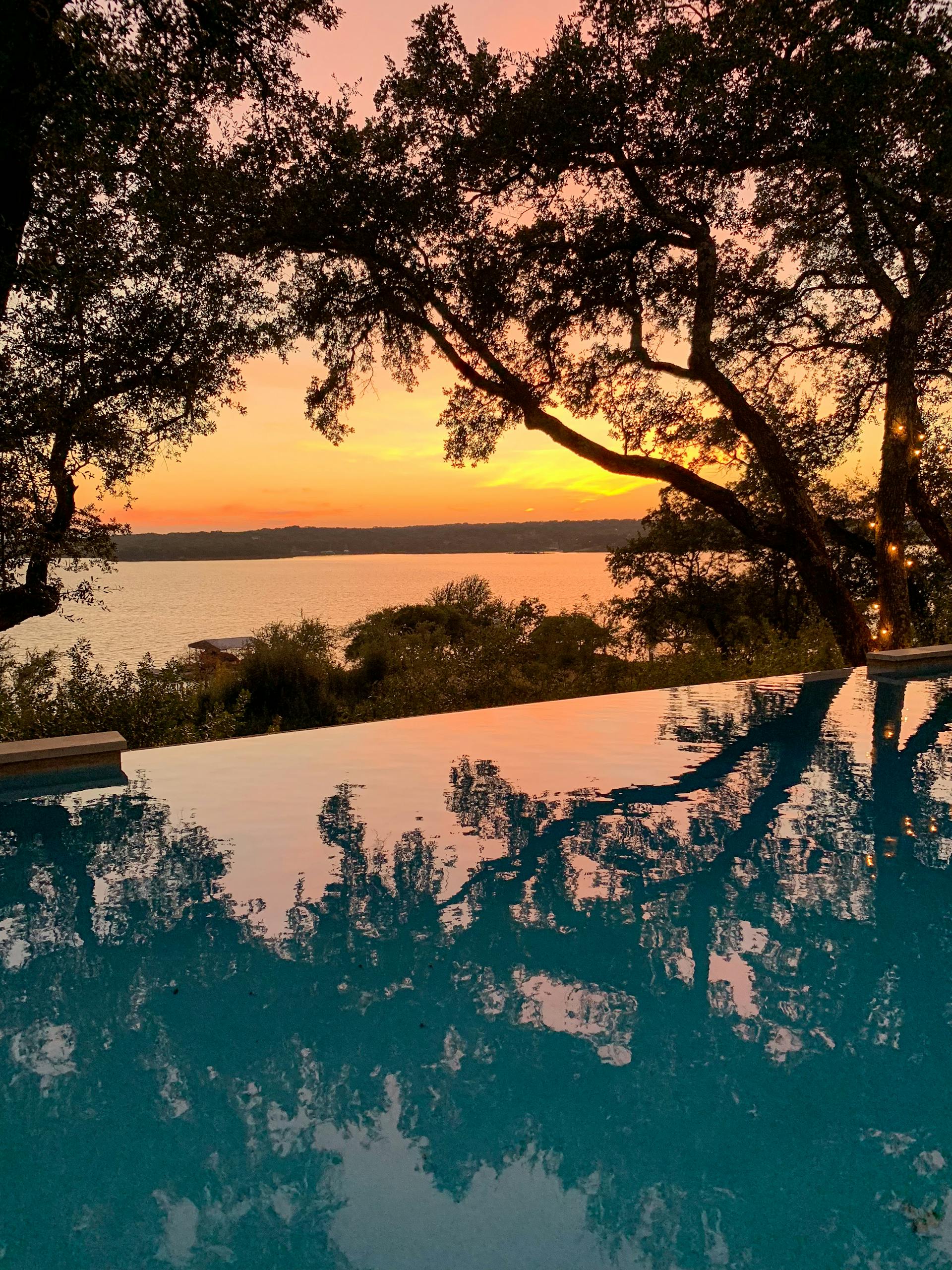 Capture the serene beauty of an Austin sunset reflecting over an infinity pool with vibrant colors.